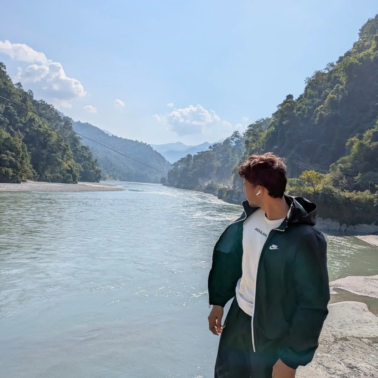 Aman looking down a wide green river between forested slopes